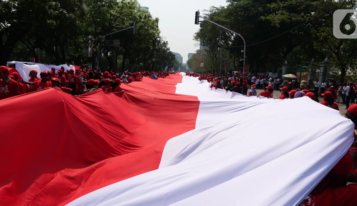 Sejumlah relawan membentangkan Bendera Merah Putih di kawasan jalan Medan Merdeka Selatan, Jakarta, Minggu (20/10/2019). Bendera Merah Putih Sekitar 200 meter dibentangkan jelang pelantikan Presiden-Wapres RI terpilih Joko Widodo-Ma'ruf Amin periode 2019-2024. (Liputan6.com/Herman Zakharia)