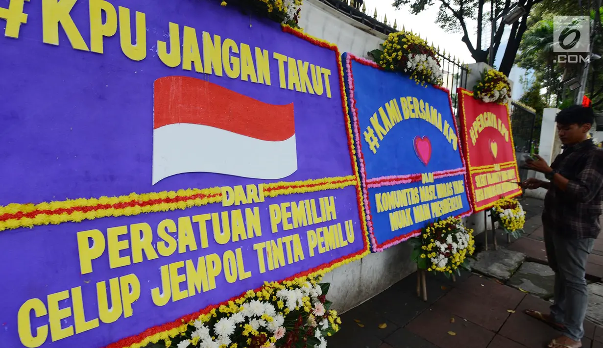 Warga berdiri dekat karangan bunga yang ada di Gedung Komisi Pemilihan Umum (KPU), Jakarta, Sabtu (20/4). Karangan bunga terus berdatangan ke Gedung KPU. (merdeka.com/Imam Buhori)