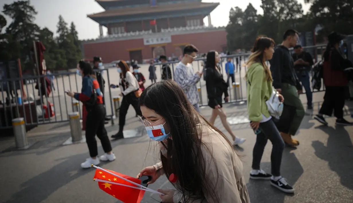 Seorang wanita mengenakan masker untuk mencegah penyebaran virus corona memegang bendera nasional Kota Terlarang selama Hari Nasional di Beijing, Rabu, (7/10/2020). Turis Tiongkok melakukan 425 juta perjalanan domestik pada paruh pertama dari delapan hari libur Hari Nasional. (AP Photo/Andy Wong)