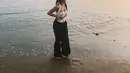 Melihat gaya chic Aaliyah Massaid main di pantai. Ia mengenakan atasan cropped bra putih dengan detail halter-neck, dipadu mengenakan celana panjang hitam. [Foto: Instagram/aaliyah.massaid]