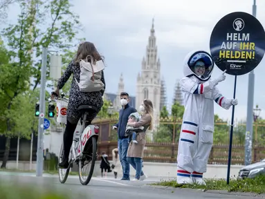 Seorang pesepeda diperlihatkan peringatan untuk mengenakan helm oleh siswa berkostum astronaut, di Ring Street, Wina, Austria, Rabu (5/5/2021). Delapan siswa Wina berpartisipasi dalam acara tersebut untuk mengingatkan pengendara sepeda mengenakan helm demi keamanan mereka. (JOE KLAMAR/AFP)