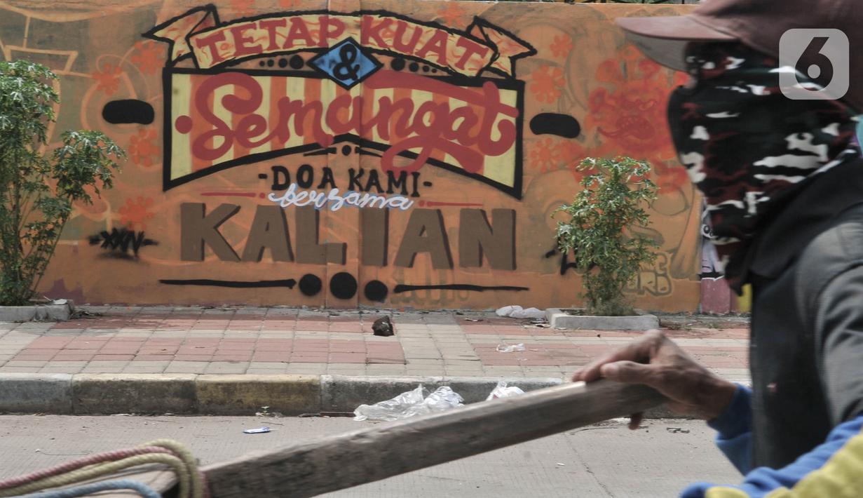 Pemulung melintas di depan mural dukungan untuk tim medis Covid-19 di kawasan Sunter, Jakarta, Rabu (27/5/2020). Mural tersebut sebagai bentuk dukungan untuk tim medis penanganan Covid-19 sekaligus mengingatkan masyarakat agar taat mengikuti aturan PSBB. (merdeka.com/Iqbal S. Nugroho)