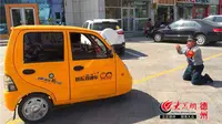 Fu Chongming terlihat tengah berlutut di depan sebuah kendaraan roda tiga untuk menghalagi pengendara dari ilegal parkir di luar toko.