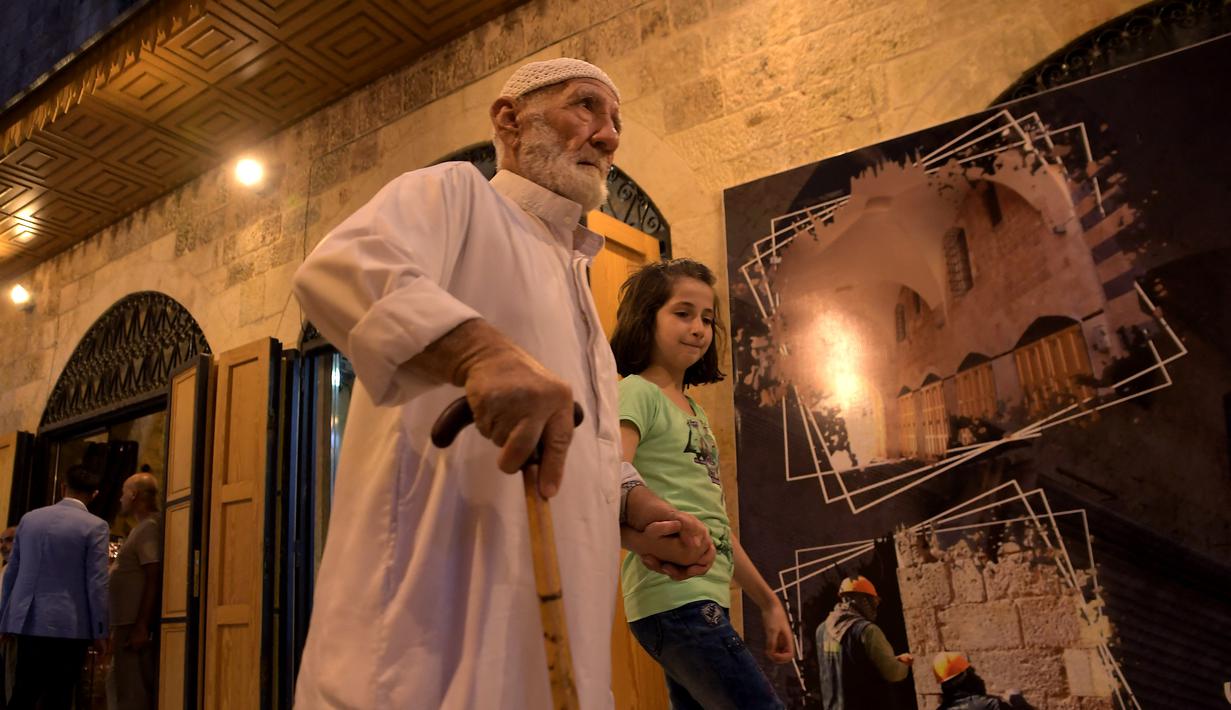 Seorang pria tua dan seorang gadis muda berjalan-jalan di "Souq Khan al-Harir" (pasar tertutup sutra) yang dibuka kembali setelah konflik bertahun-tahun di kota utara Aleppo, Suriah (29/8/2021). (AFP Photo)