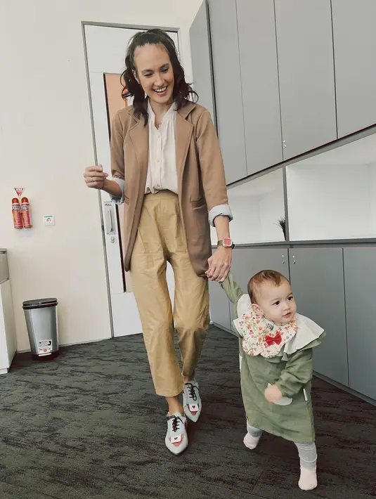Kali ini, Nadine tampil dengan workwear, diserasikan dengan nuansa warna outfit sang buah hati. Nadine mengenakan blouse putih, yang dilapisi dengan blazer cokelat, dipadu celana panjang berwarna khaki, menggandeng sang anak yang mengenakan dress lengan panjang berwarna hijau, dengan detail kerah yang gemas. Foto: Instagram.