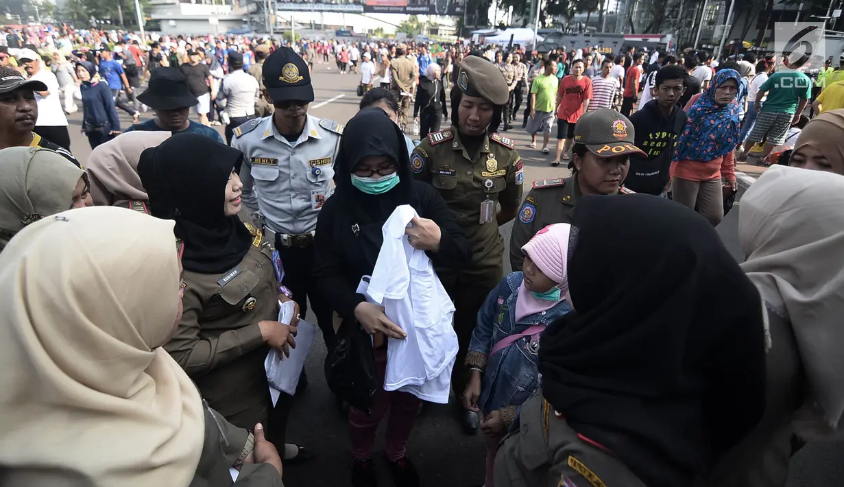 Petugas Satpol PP meminta pengunjung mengganti pakaian bertagline '#2019GantiPresiden' yang dikenakannya selama car free day (CFD), Jakarta, Minggu (6/5). Pelarangan tersebut diberlakukan sesuai Pergub No 12 Tahun 2016. (Merdeka.com/Iqbal Nugroho)