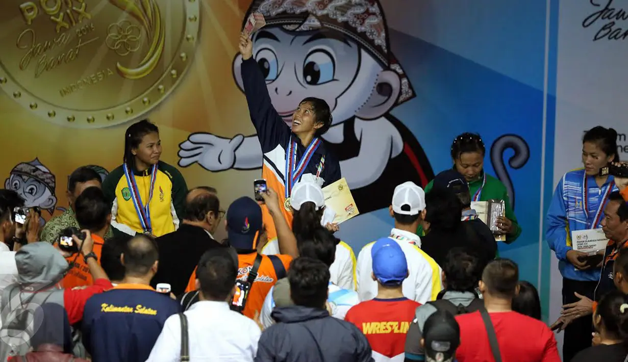 Pegulat putri Kalimantan Selatan Ridha W (tengah) mengangkat uang bonus usai memenangi laga final gaya bebas kelas 63 kg putri melawan Anita (Kaltim) pada PON XIX di Arena Saparua Sport Park, Bandung, Sabtu (24/9). (Liputan6.com/Helmi Fithriansyah)