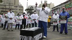 Petugas kesehatan berdiri di sekitar peti mati tiruan yang bertuliskan "Korupsi" dalam bahasa Spanyol saat memprotes kurangnya peralatan pelindung bagi mereka yang merawat pasien COVID-19, di luar rumah sakit umum di Lima, Peru (29/9/2020). (AP Photo/Martin Mejia)