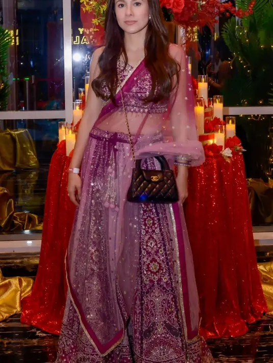 Wulan Guritno mengenakan lehenga warna keunguan dengan atasan crop berbordir silver senada rok panjang, lengkap dengan selendangnya. Ia pun membawa tas Chanel hitam. Wulan juga mengenakan bindi merah dan rambut panjang coklat terurai. [@wulanguritno]