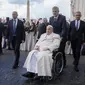 Paus Fransiskus dibantu oleh ajudannya saat audiensi publik di St. Peter's Square di Vatikan, Rabu 6 Maret 2024, ia tak bisa naik mobil kepausan sehingga memilih kursi roda. (AP/Gregorio Borgia)