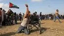 Seorang pria Palestina bernama Saber al-Ashkar melemparkan batu bersanggakan kursi rodanya saat terlibat bentrok dengan pasukan Israel di dekat perbatasan antara Israel dengan Jalur Gaza (11/5). (AFP/Mahmud Hams)