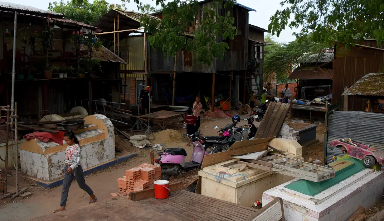 Seorang wanita melewati bangunan rumah di sebuah kuburan di Phnom Penh, Kamboja pada 21 Mei 2019. Pemakaman menjadi tempat peristirahatan abadi bagi orang mati, tetapi area pemakaman ini menjelma sebagai tempat tinggal untuk bertahan hidup bagi mereka yang didera kemiskinan. (TANG CHHIN Sothy/AFP)