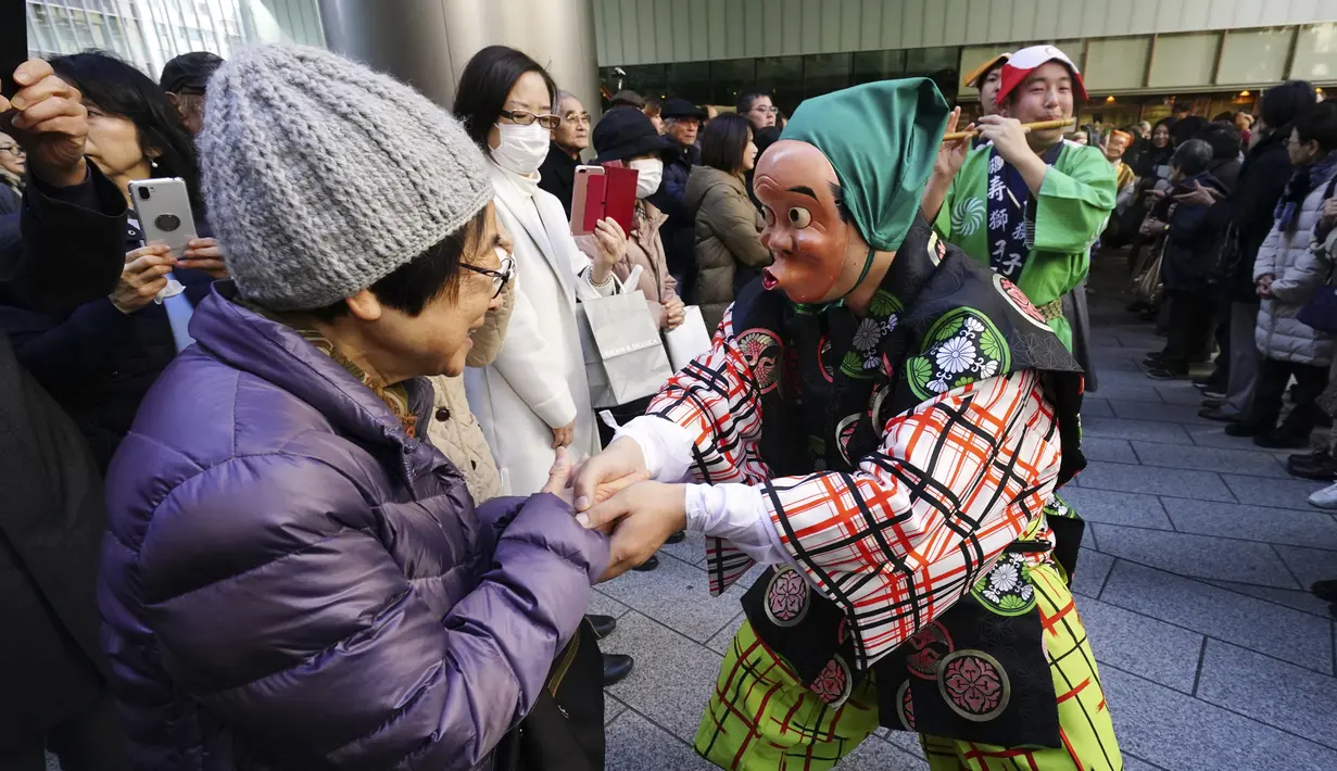 Seniman mengenakan topeng badut tradisional Jepang berjabat tangan dengan warga selama Festival Konpira di kuil Kotohiragu di distrik bisnis Toranomon, Tokyo  (10/1/2020). Kehadiran para seniman ini sukses menarik perhatian warga. (AP Photo/Eugene Hoshiko)