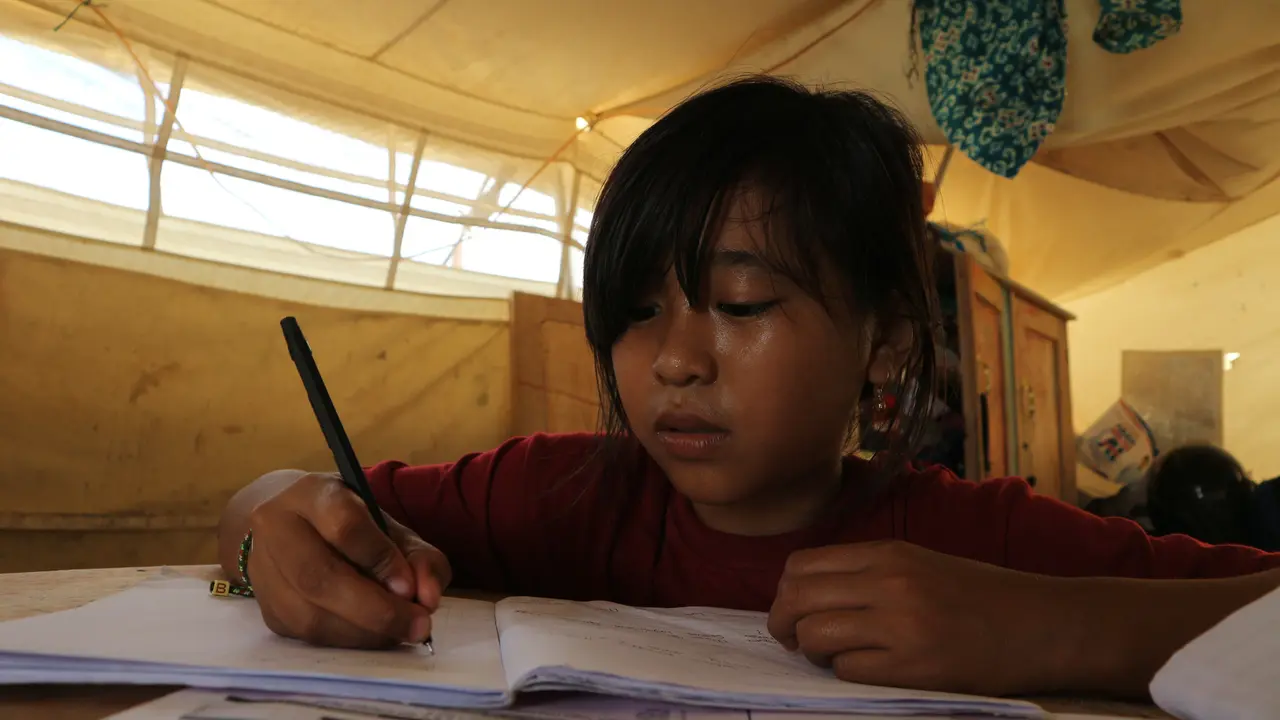 Dinar sedang mengerjakan tugas sekolah di tenda daruratnya di Kelurahan Balaroa, Palu Barat, Rabu (18/3/2020). (foto: Liputan6.com/Heri Susanto).