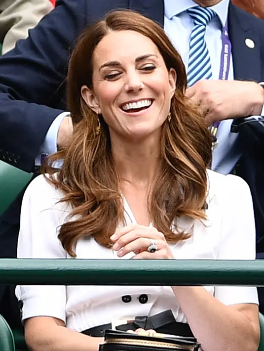 Kate Middleton tertawa saat menyaksikan pertandingan turnamen tenis Wimbledon 2019 di All England Tennis Club di Wimbledon, London, Inggris 2/7/2019). Kate Middleton bergaun gaun putih dari Suzannah dan tas tangan Alexander McQueen dan kacamata hitam Ray-Ban. (AFP Photo/Glyn Kirk)