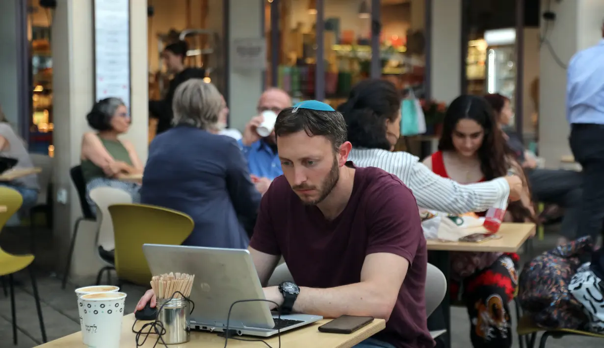 Seorang pria mengecek laptopnya di kafe di Abima Square di kota Tel Aviv, Israel (20/5/2021).  Israel dan dua kelompok bersenjata utama Palestina di Gaza, Hamas dan Jihad Islam, menyetujui gencatan senjata untuk mengakhiri konflik selama 11 hari. (AFP/Gideon Markowicz)