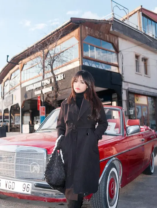 Gaya liburan keren ala Fuji pakai turtleneck dan coat, serta menenteng tas yang semuanya berwarna hitam. [Foto: Instagram/fuji_an]
