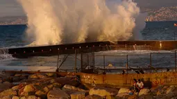 Pasanganduduk di batu sambil meminum kopi ketika ombak menerjang garis pantai Beirut, Lebanon, (26/10). (AP Photo / Hussein Malla)