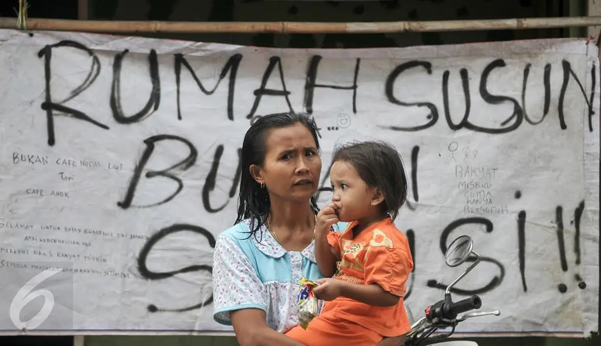 Seorang ibu menggendong anaknya berdiri di depan spanduk penolakan penggusuran kawasan Bukit Duri, Jakarta, Rabu (28/9). Pemprov DKI akhirnya melakukan penertiban pemukiman di Bukit Duri terkait revitalisasi sungai Ciliwung. (Liputan6.com/Yoppy Renato)