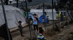 Anak-anak imigran bermain di sebelah pagar di luar kamp pengungsi di pulau Samos, Yunani (13/11/2019). Kamp Samos, awalnya dibangun untuk menampung 650 orang, telah lama melampaui batas-batasnya. (AFP Photo/Angelos Tzortzinis)