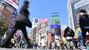 Orang-orang melintasi persimpangan pejalan kaki yang terkenal di distrik Shibuya, Tokyo pada 20 Maret 2019. Persimpangan jalan ini menjadi salah satu persimpangan terbesar dan tersibuk di dunia. (Photo by CHARLY TRIBALLEAU / AFP)