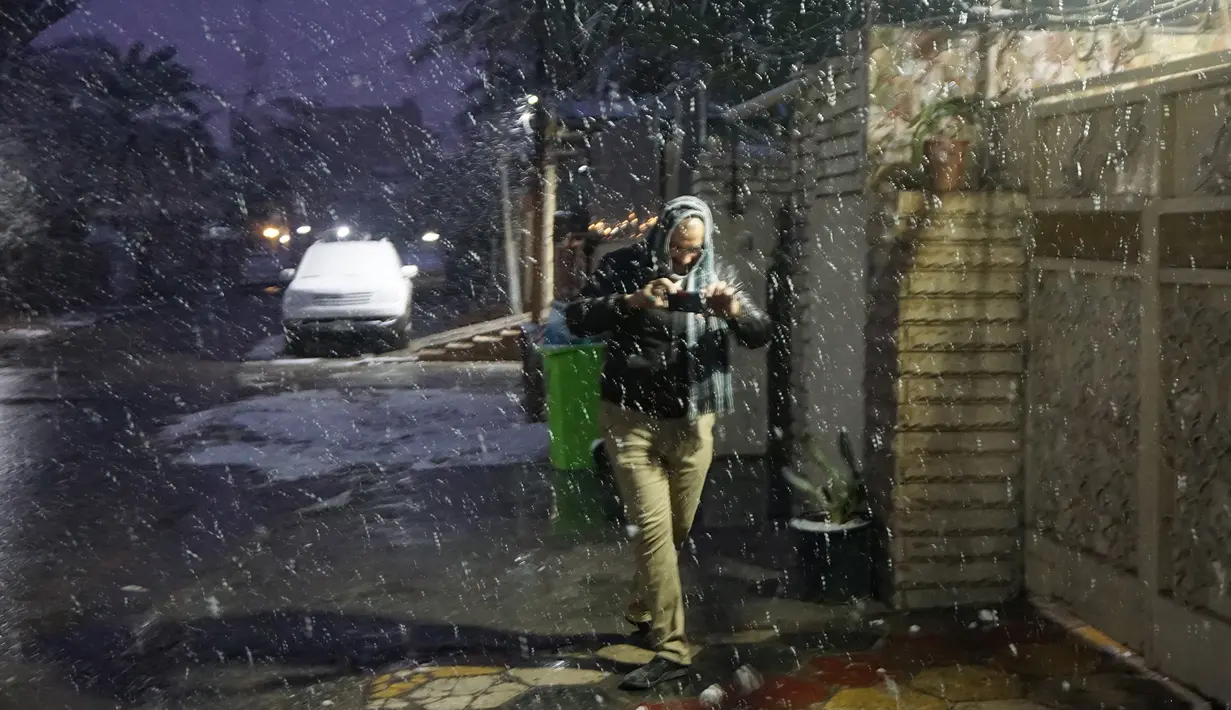 Seorang pria mengambil foto dengan smartphonenya saat salju turun di Baghdad, Selasa (11/2/2020). Salju turun di Baghdad untuk pertama kalinya dalam satu dekade setelah sebelumnya ibu kota Irak itu sempat diguyur salju pada 2008, tetapi hanya berlangsung sekejap dan langsung mencair (SABAH ARAR/AFP)