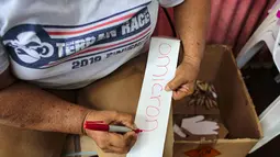 Seorang perempuan menulis kata "Omicron" di selembar kertas yang akan ditempelkan pada boneka buatan tangan di Managua, Nikaragua, Senin (27/12/2021). Boneka-boneka itu dibakar pada 31 Desember tengah malam sebagai tradisi mengucapkan selamat tinggal pada tahun yang lama. (OSWALDO RIVAS/AFP)