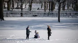 Sebuah keluarga berdiri di lapangan tertutup salju di Central Park setelah badai salju pertama musim dingin 2022 di New York City, Jumat (7/1/2022). Badai musim dingin membawa lebih dari 15 cm salju di bagian timur Amerika Serikat (AS), menutup sekolah, kantor dan jalan-jalan. (Ed JONES / AFP)