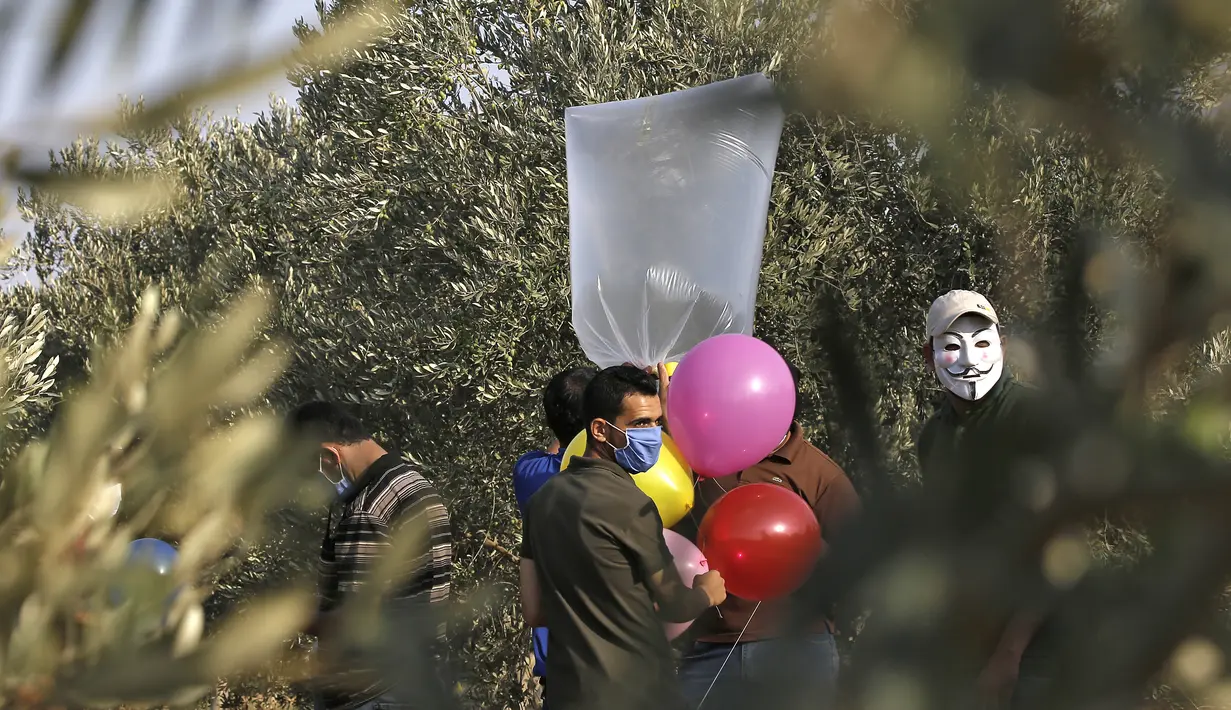 Sejumlah pria Palestina menyiapkan balon dengan alat peledak yang akan diterbangkan ke arah Israel di dekat kamp pengungsi al-Bureij, sepanjang perbatasan Israel- Jalur Gaza (12/8/2020). (AFP Photo/Mohammed Abed)