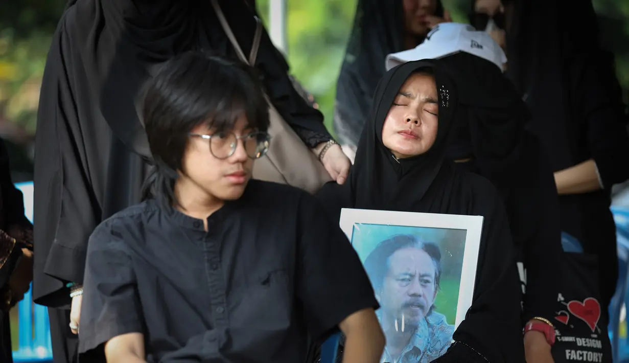 Tubuhnya yang tak berdaya, terus mendekap erat foto suami di sepanjang perjalanan menuju liang lahad. Tampak dalam foto, Karina Ranau (kanan) sesaat sebelum pemakaman suaminya, Epy Kusnandar, di Tempat Pemakaman Umum (TPU) Jeruk Purut, Jakarta Selatan, Kamis (4/12/2025) pagi. (Kapanlagi.com/Budy Santoso)