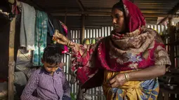 Imradul Ali (10) memakai kemeja saat ibunya Anuwara Beghum (30) menuangkan minyak rambut ke kepalanya saat akan ke sekolah, di kamar sewaan mereka di Gauhati, India (5/2/2021).  Ali berasal dari keluarga yang sebagian besar mata pencahariannya bekerja sebagai pemulung. (AP Photo/Anupam Nath)
