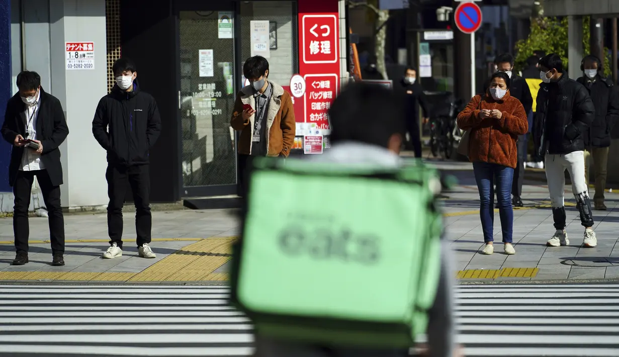 Orang-orang mengenakan masker untuk mencegah penyebaran virus corona menunggu lampu lalu lintas di persimpangan di Tokyo (8/2/2021). Ibukota Jepang mengonfirmasi lebih dari 270 kasus virus korona baru pada hari Senin. (AP Photo/Eugene Hoshiko)