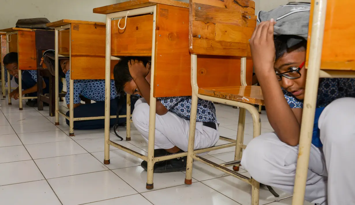 Sejumlah siswa berlindung di bawah meja saat simulasi bencana gempa dan tsunami di sebuah sekolah di Banda Aceh, Aceh, Rabu (9/10/2019). Simulasi dilakukan karena Aceh merupakan daerah rawan kedua bencana tersebut dan turut merusak bangunan sekolah. (Photo by CHAIDEER MAHYUDDIN / AFP)