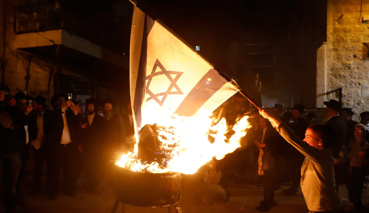 Seorang bocah Yahudi ultra ortodoks antizionis membakar bendera Israel di Yerusalem ultra-Ortodoks Mea Shearim, Rabu (2/5). Hal itu dilakukan selama perayaan Hari Raya Yahudi Lag BaOmer. (MENAHEM KAHANA / AFP)