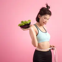 Seorang perempuan sedang mengukur lingkar tubuhnya sambil memegang semangkuk salad (Foto Dok: Freepik/jcomp).