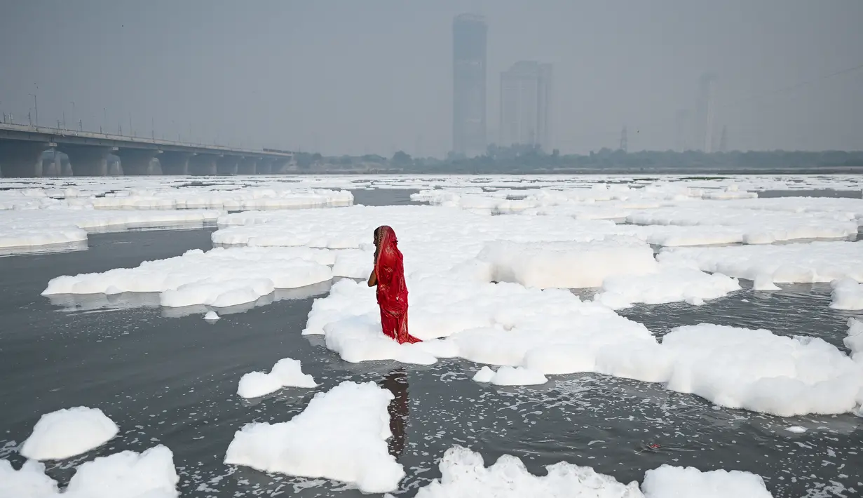 Seorang wanita mandi di sungai Yamuna yang tertutup busa limbah sebagai bagian dari ritual untuk festival Chhath Puja yang akan datang di New Delhi, Senin (8/11/2021). Sungai yang sangat dianggap suci oleh umat Hindu India ini dipenuhi lapisan busa karena limbah beracun. (Sajjad HUSSAIN / AFP)