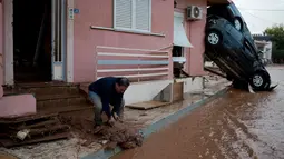 Seorang pria membersihkan lumpur dekat mobil yang tersangkut di tembok rumahnya usai banjir bandang melanda kota industri Mandra, barat Athena, Rabu (15/11). Setidaknya 15 orang tewas akibat diterjang banjir yang melanda Yunani. (AP/Petros Giannakouris)