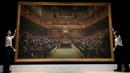 Petugas menata lukisan seniman jalanan Banksy yang dipajang di ruang lelang Sotheby, London, Jumat (27/9/2019). Lukisan dengan objek 100 simpanse yang duduk di parlemen Inggris tersebut pernah menghebohkan publik. (AP/Kirsty Wigglesworth)