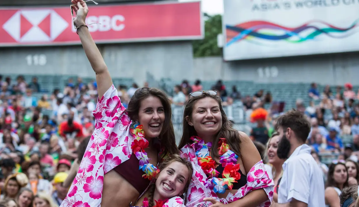 Tiga wanita tersenyum saat menyaksikan hari pertama turnamen rugby sevens Hong Kong, China (6/4). Turnamen ini diadakan setiap tahun di Hong Kong pada akhir pekan di akhir Maret atau awal April. (AFP Photo/Isaac Lawrence)
