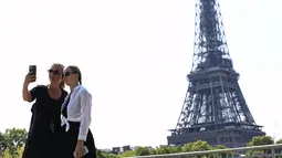 Wisatawan berfoto dengan latar belakang dekat Menara Eiffel di Paris, Rabu (31/8/2022). Kerumunan orang memadati landmark Paris dan pantai Riviera, terutama berkat masuknya orang Amerika yang mendapat manfaat dari euro yang lemah. (AP Photo/Aurelien Morissard)