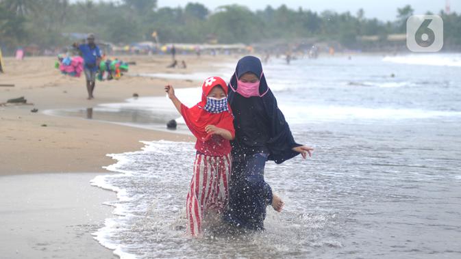 Anak-anak yang mengenakan masker bermain air saat mengunjungi Pantai Anyer di Cilegon, Banten, Minggu (25/10/2020). Akhir pekan dimanfaatkan warga Jakarta dan sekitarnya untuk berwisata dengan tetap menerapkan protokol kesehatan Covid-19. (merdeka.com/Arie Basuki)