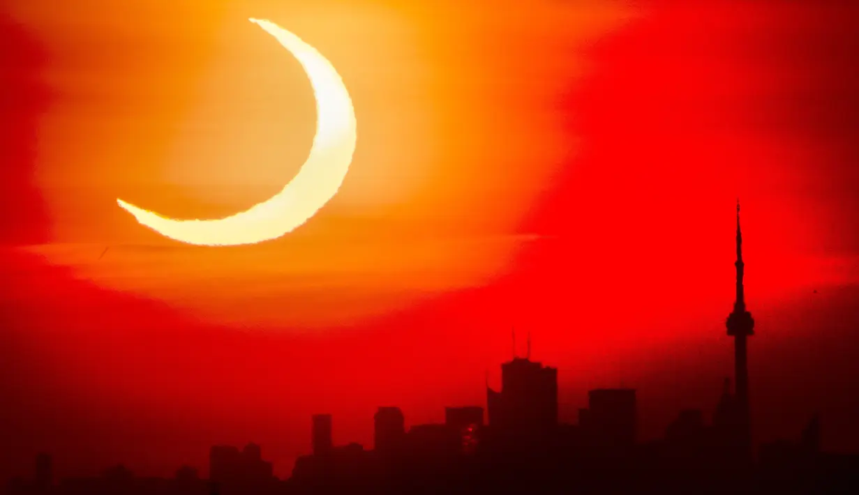 Gerhana matahari cincin muncul di atas cakrawala Toronto, Kamis (10/6/2021). Fenomena gerhana matahari cincin jatuh pada 10 Juni 2021. Gerhana matahari cincin menjadi fenomena yang dinanti setelah gerhana Bulan total pada 26 Mei 2021 lalu.  (Frank Gunn/The Canadian Press via AP)