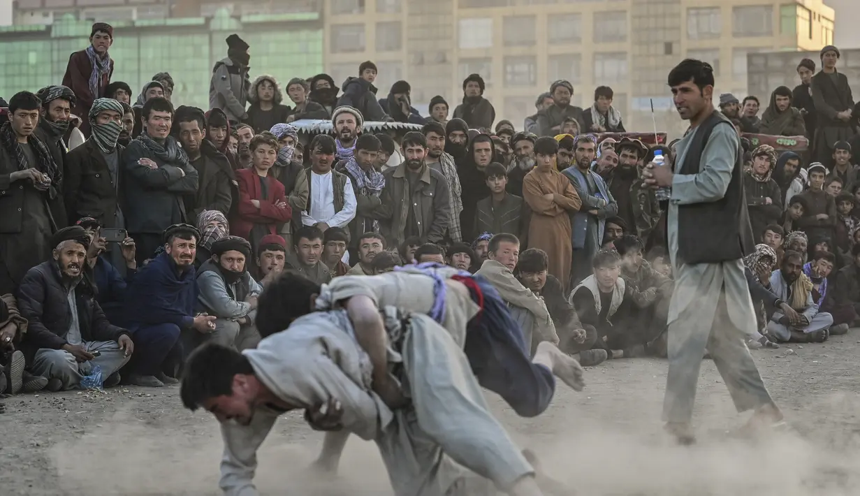 Pria Afghanistan bergulat di latar belakang selama tontonan gulat mingguan yang diadakan di arena darurat di taman Chaman-e-Hozori, di Kota Kabul (12/11/2021). (AFP/Hector Retamal)