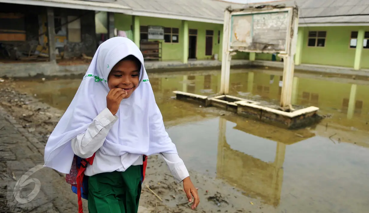 Siswa MI Mansyaul Huda melewati pelataran sekolah yang terkena dampak abrasi pantai Muara Gembong, Bekasi, Selasa, (26/7). Tingkat abrasi yang tinggi menyebabkan sejumlah rumah terkikis dan beberapa sekolah terendam air laut. (Liputan6.com/Gempur M Surya)