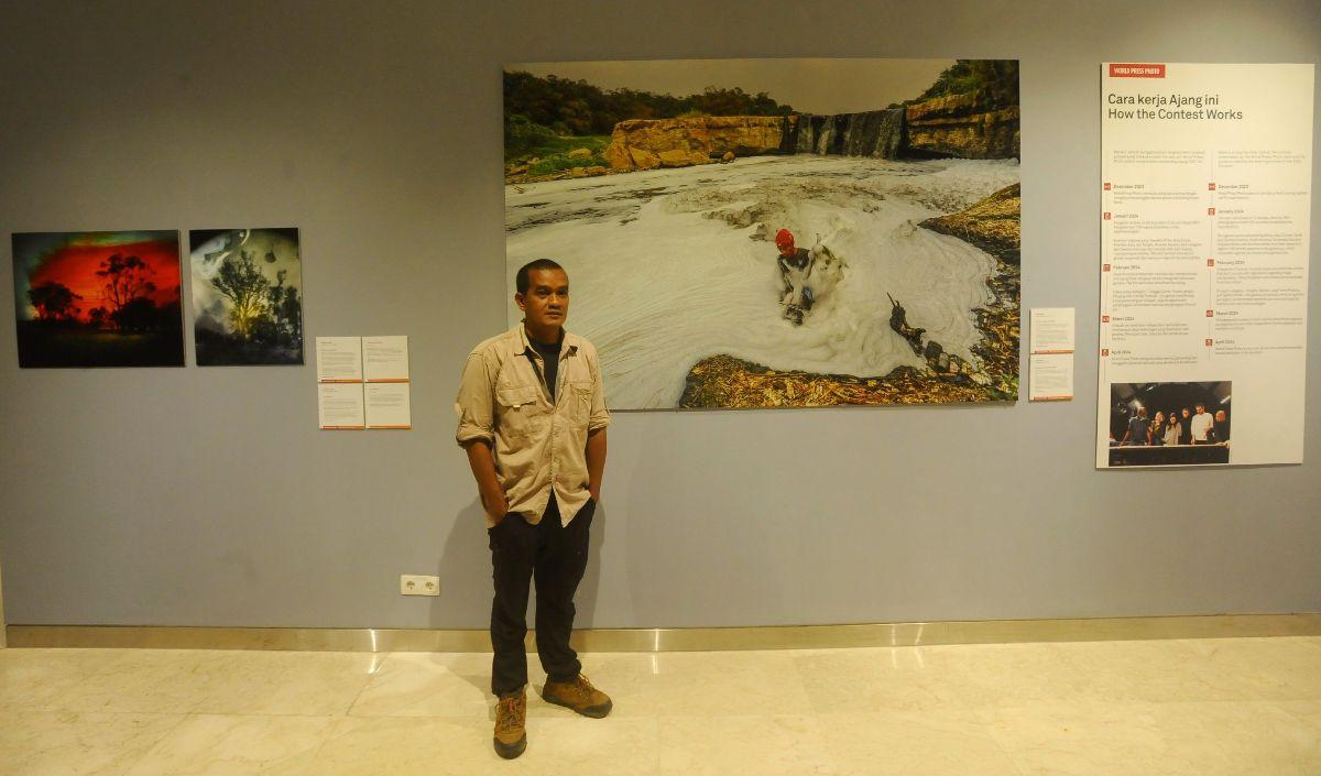 Pewarta Foto Merdeka.com, Arie Basuki berpose di depan karyanya yang berjudul &ldquo;Pollution in the Cileungsi River&rdquo; saat pameran World Press Photo (WPP) 2024 di Pusat Kebudayaan Belanda Erasmus Huis, Jakarta, Sabtu (24/8/2024).&nbsp;<br>