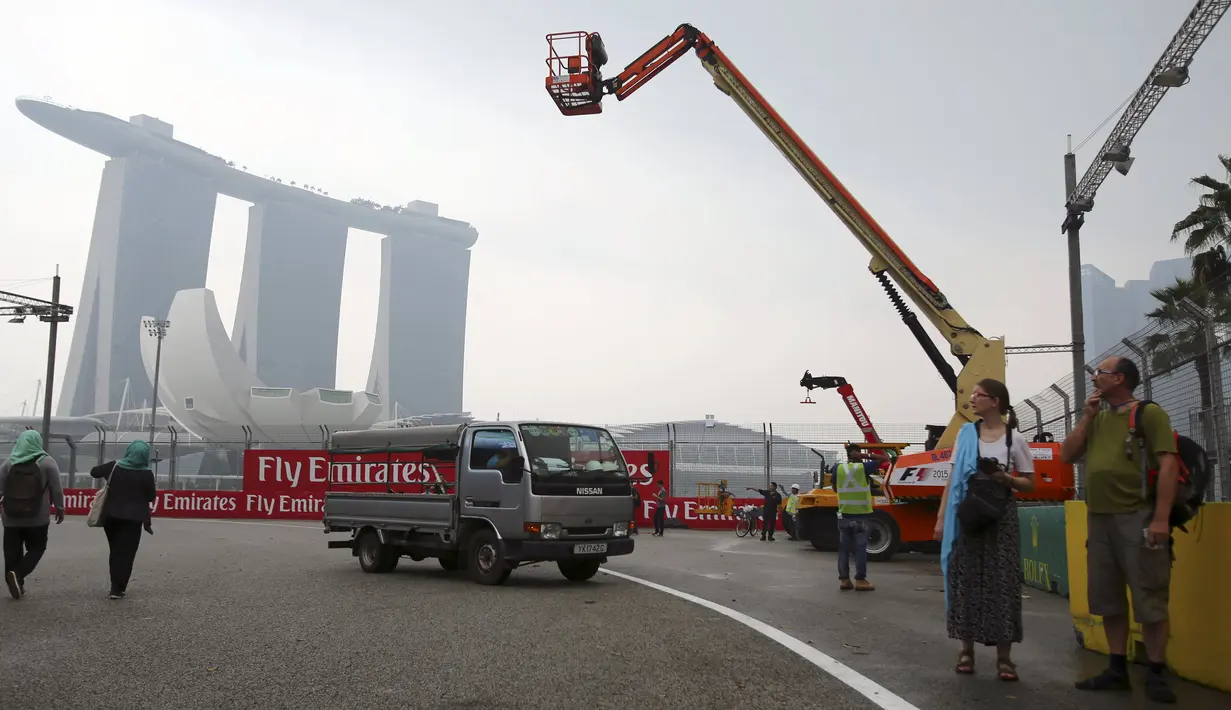 Turis berjalan di sirkuit Marina Bay yang tertutup asap tebal sebelum kejuaraan F1 grand prix dimulai, Singapura, Rabu (16/9/2015). Panitia mengakhawatirkan kabut asap yang tebal berdampak pada F1 Grand Prix Minggu nanti. (REUTERS/Tim Chong)