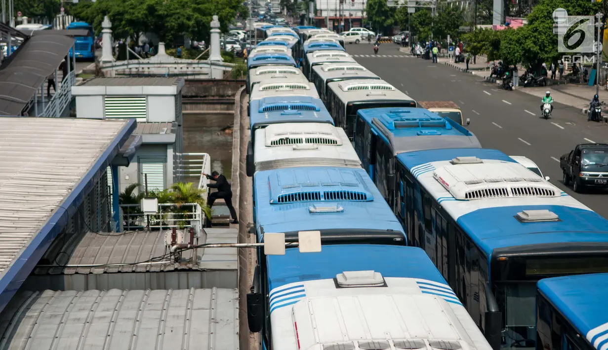 Seorang warga melewati Bus Transjakarta mogok kerja mengantarkan penumpang di Halte Harmoni, Jakarta (12/6). Para supir menuntut penghapusan kontrak yang bertahun-tahun serta meminta pengangkatan karyawan tetap. (Liputan6.com/Gempur M Surya)