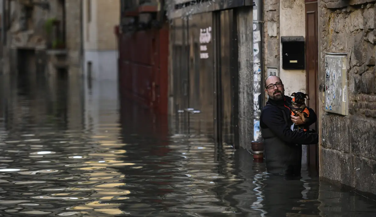 Seorang pria membawa hewan peliharaannya di depan rumahnya melalui daerah banjir di dekat Sungai Ebro di Tudela, Spanyol utara (12/12/2021). Hujan deras menyebabkan banjir di Spanyol utara. (AP Photo/Alvaro Barrientos)