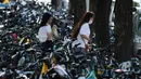 Dua orang wanita berjalan melintasi sepeda-sepeda yang diparkir memenuhi trotoar di Beijing, China (21/7/2020). Selama dua tahun terakhir, Pemerintah Beijing telah menyediakan fasilitas persewaan sepeda menggunakan sistem bike sharing. (AFP Photo/Greg Baker)