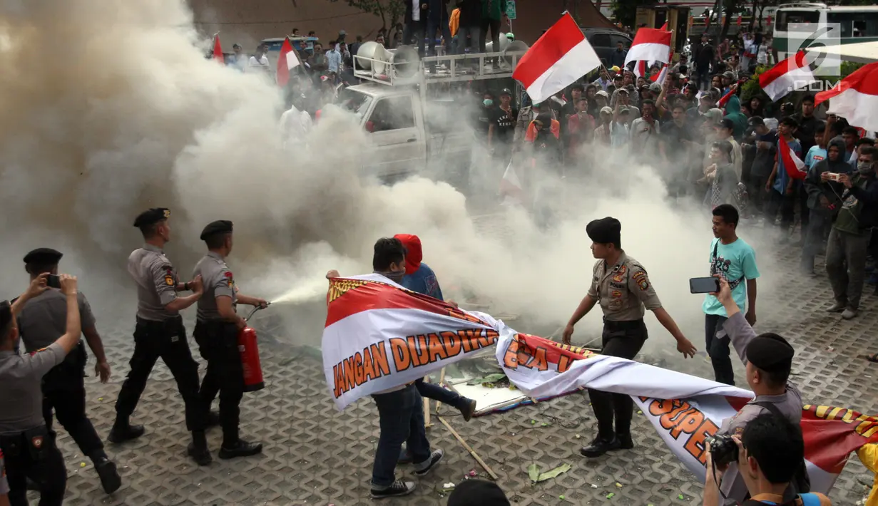 Aparat kepolisian memadamkan api dari karangan bunga yang dibakar oleh massa di Gedung KPK, Jakarta, Jumat (13/9/2019). Sempat terjadi baku hantam dalam demo tersebut saat massa pendukung dari revisi UU KPK mencoba merangsek untuk mencopot kain hitam yang menutupi logo KPK. (Liputan6.com/HO/Andri)